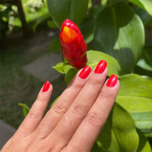 hand with nails painted in mandarin non toxic nail polish next to red flower bloom
