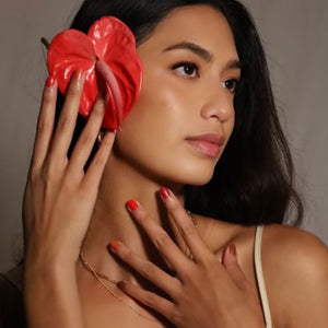 women wearing multiple red colors of kapa nui non toxic nail polish with red flower in her ear
